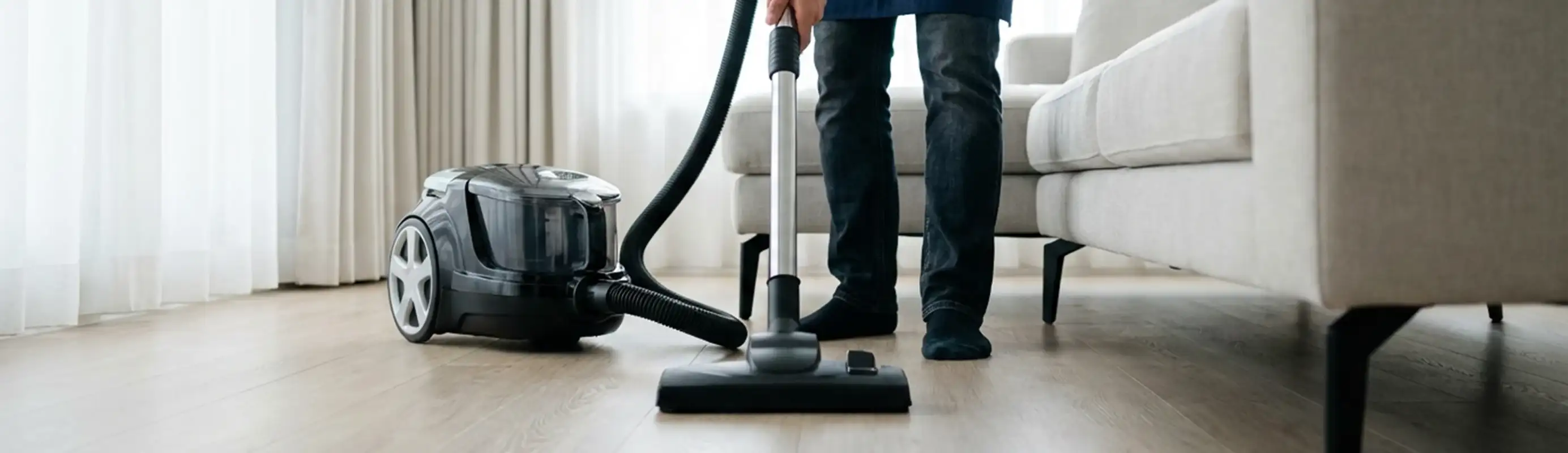 Professional house cleaner vacuuming a living room floor with a canister vacuum cleaner, Newark, NJ.