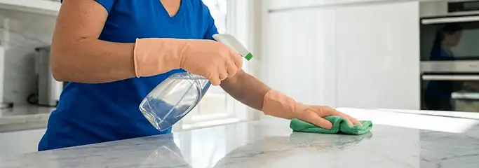 Maid service worker spraying and wiping a kitchen countertop with a microfiber cloth for sanitizing, Newark, NJ.