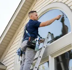 Professional window cleaner on a ladder using a squeegee to clean an exterior arched window, Newark, NJ.