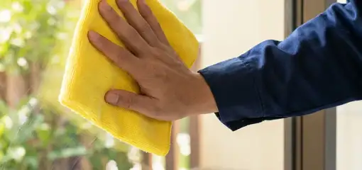 House cleaner wiping a glass window with a yellow microfiber cloth for streak-free cleaning, Newark, NJ.